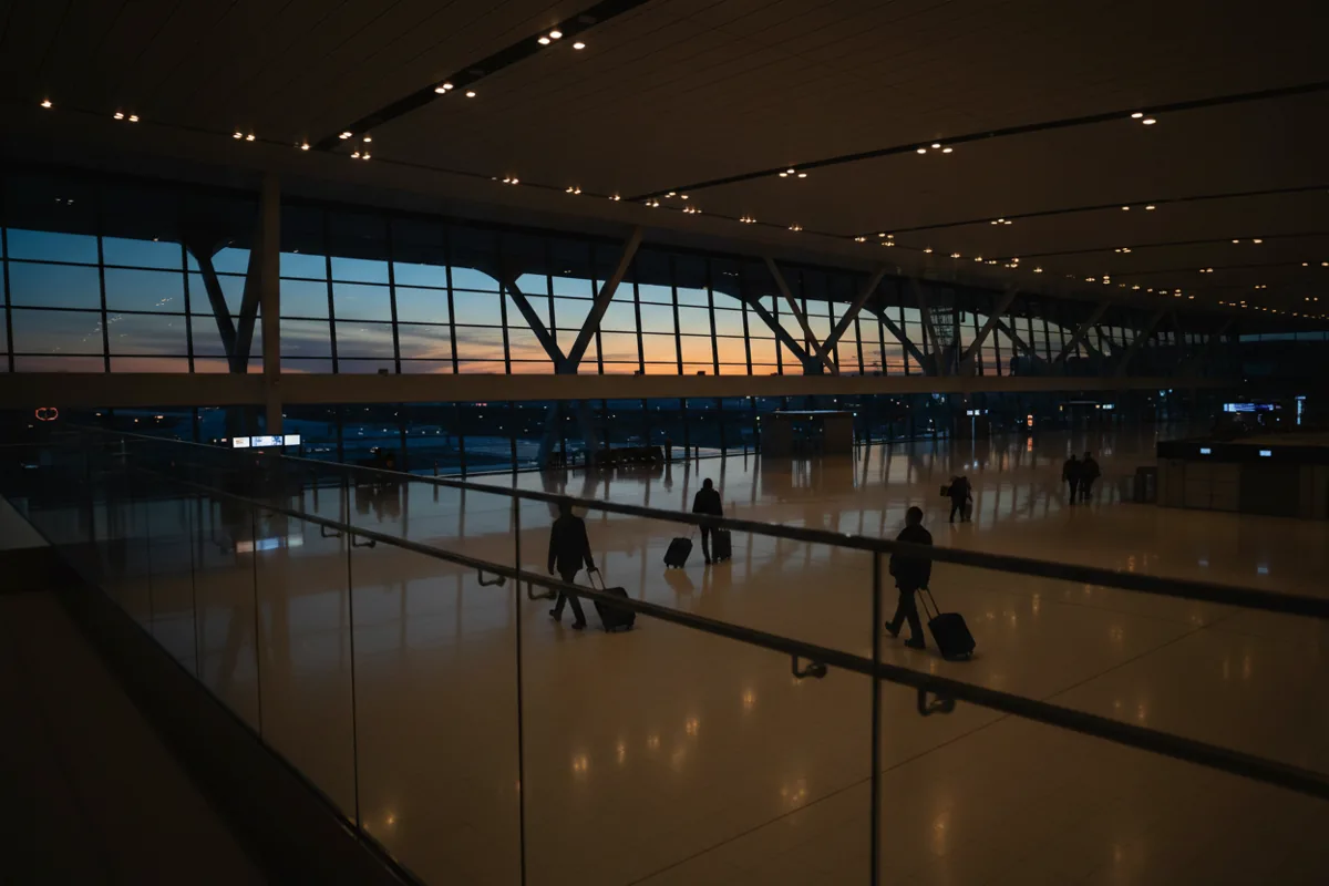 A spacious, modern airport departure hall with warm lighting, viewed from an upper level.