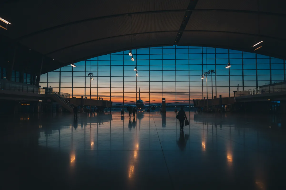 A modern, spacious airport terminal at dusk with a large airplane visible through the windows.