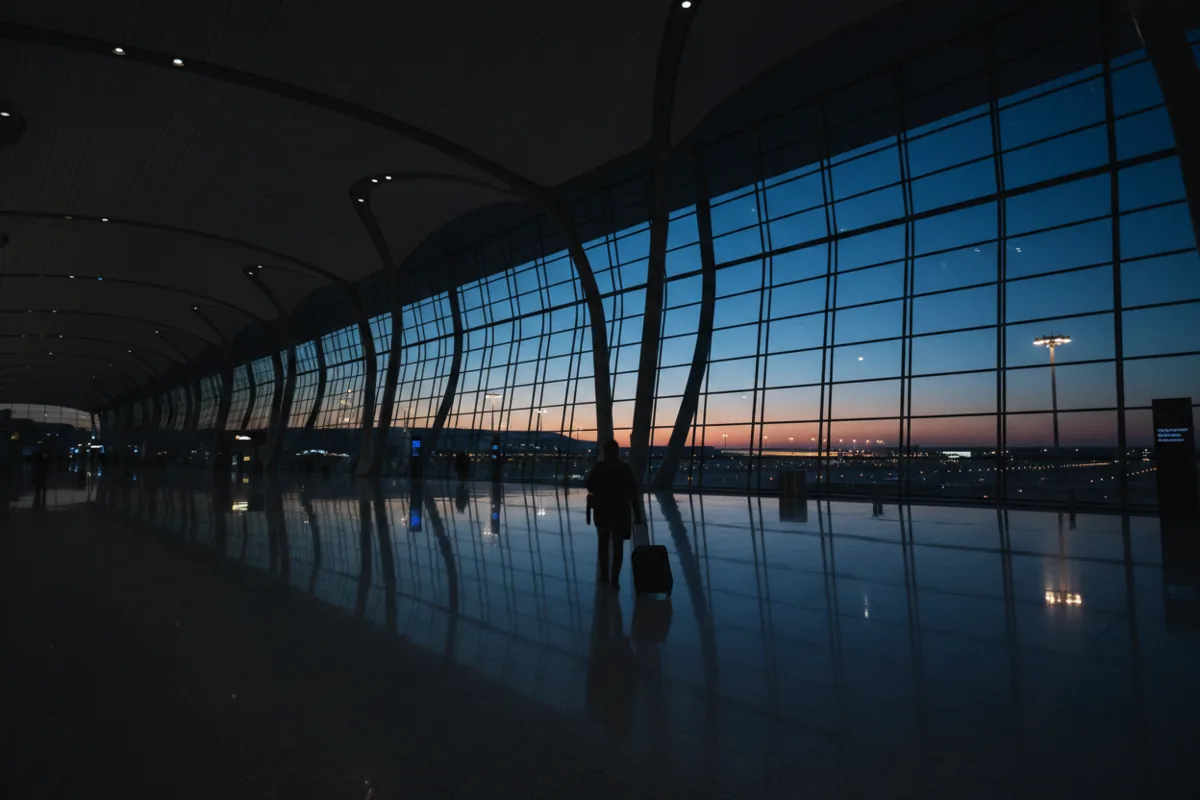 A traveler with a suitcase walks through a modern airport terminal at twilight.