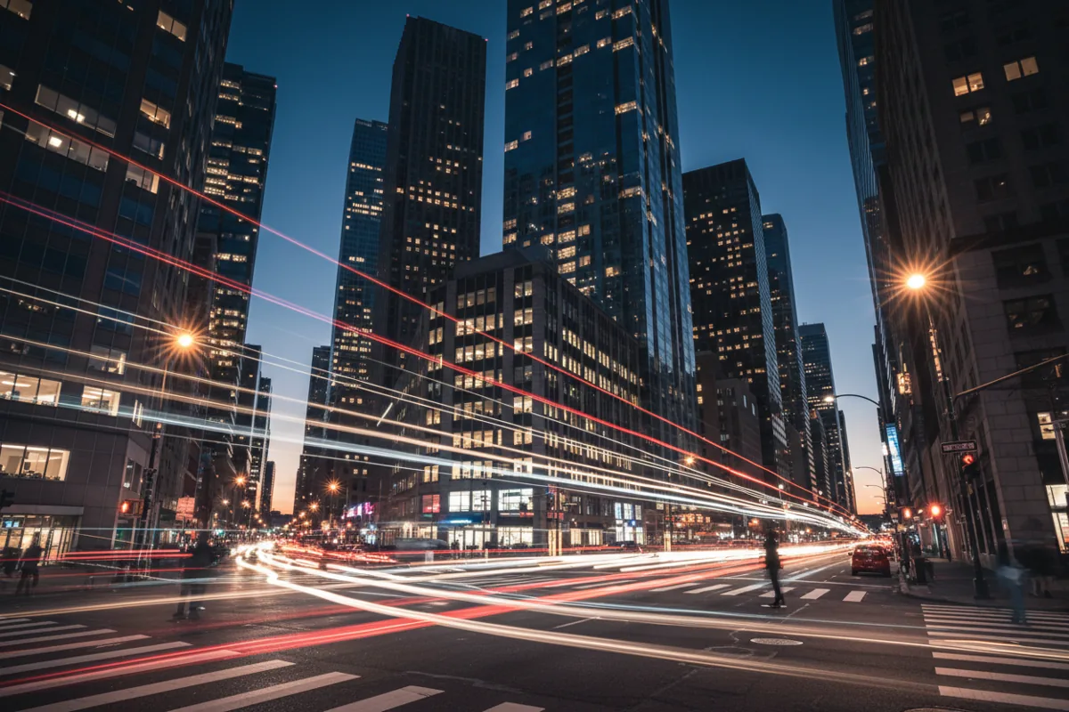 Long exposure shot of car light trails on a busy city street at night, surrounded by tall buildings.