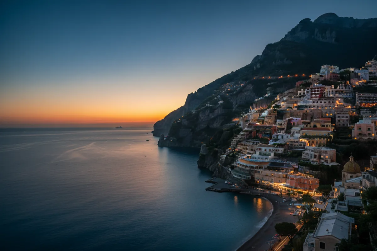 A Mediterranean coastal village with glowing lights nestled in cliffs at dusk.