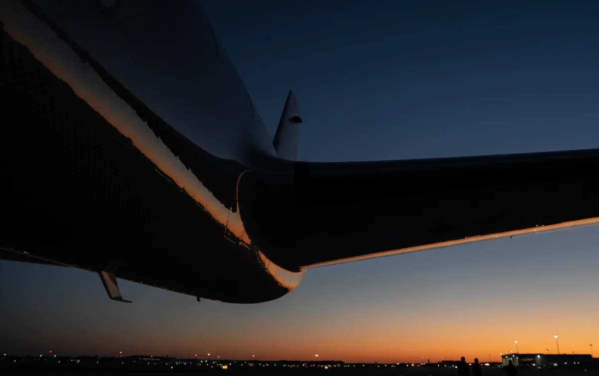 Close-up on the sleek, curved fuselage and wing of a modern private jet at sunset.