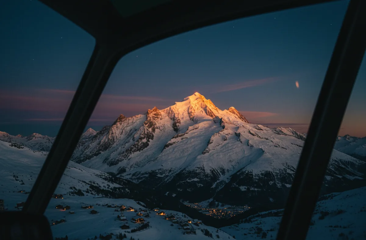 View of a snowy mountain peak at sunset from a helicopter window.