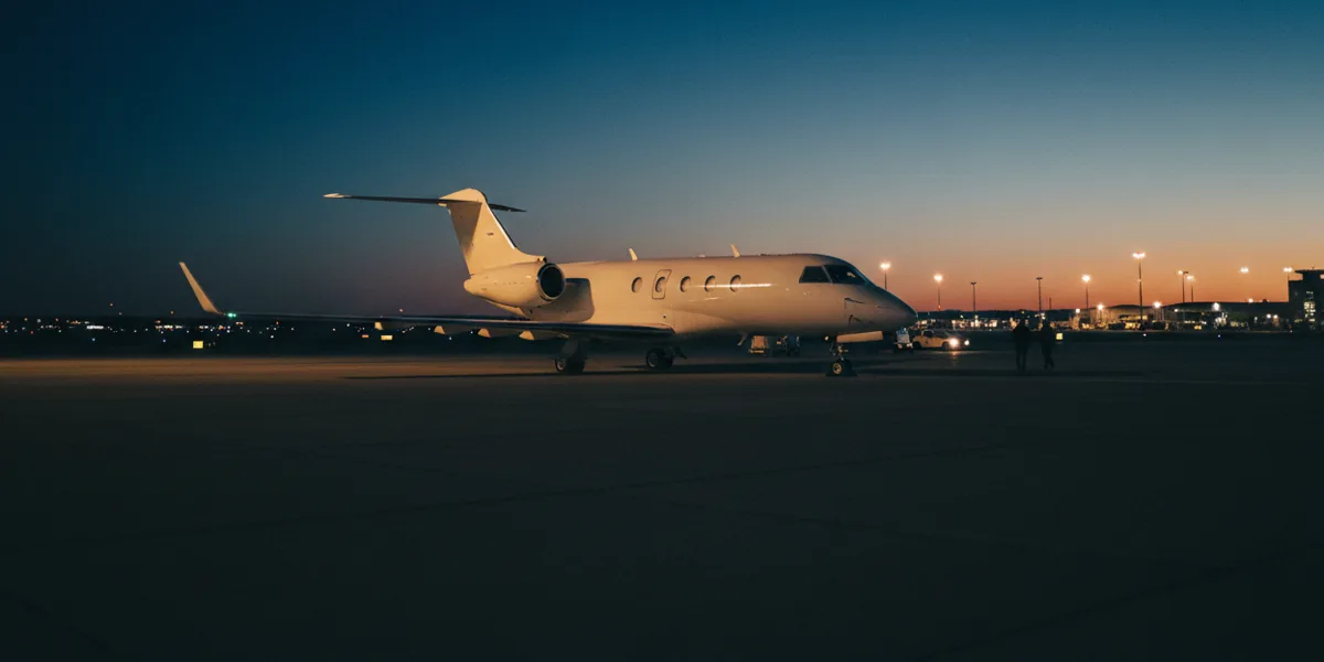 A white private jet parked on a quiet airport tarmac at sunrise.