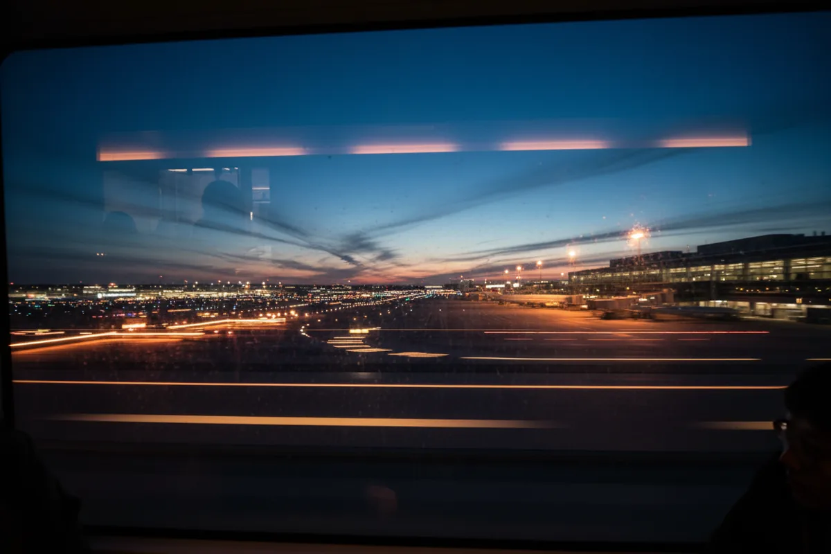 View of a glowing airport tarmac at dusk from a moving tram window.
