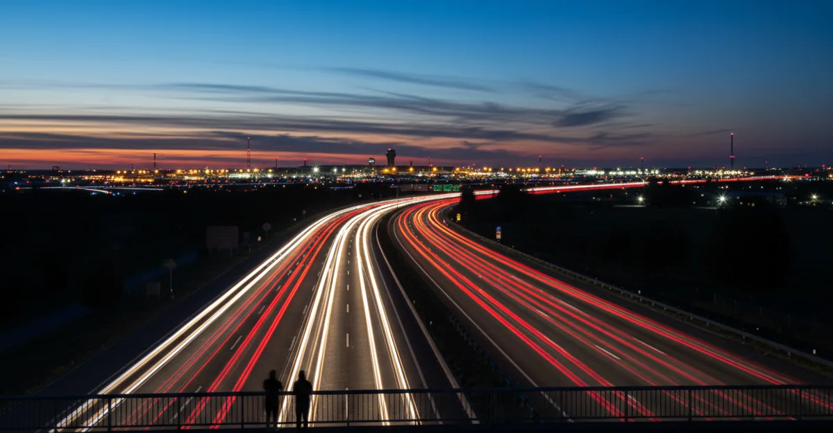 Long-exposure photo showing streaks of car lights on a highway leading to an airport at night.
