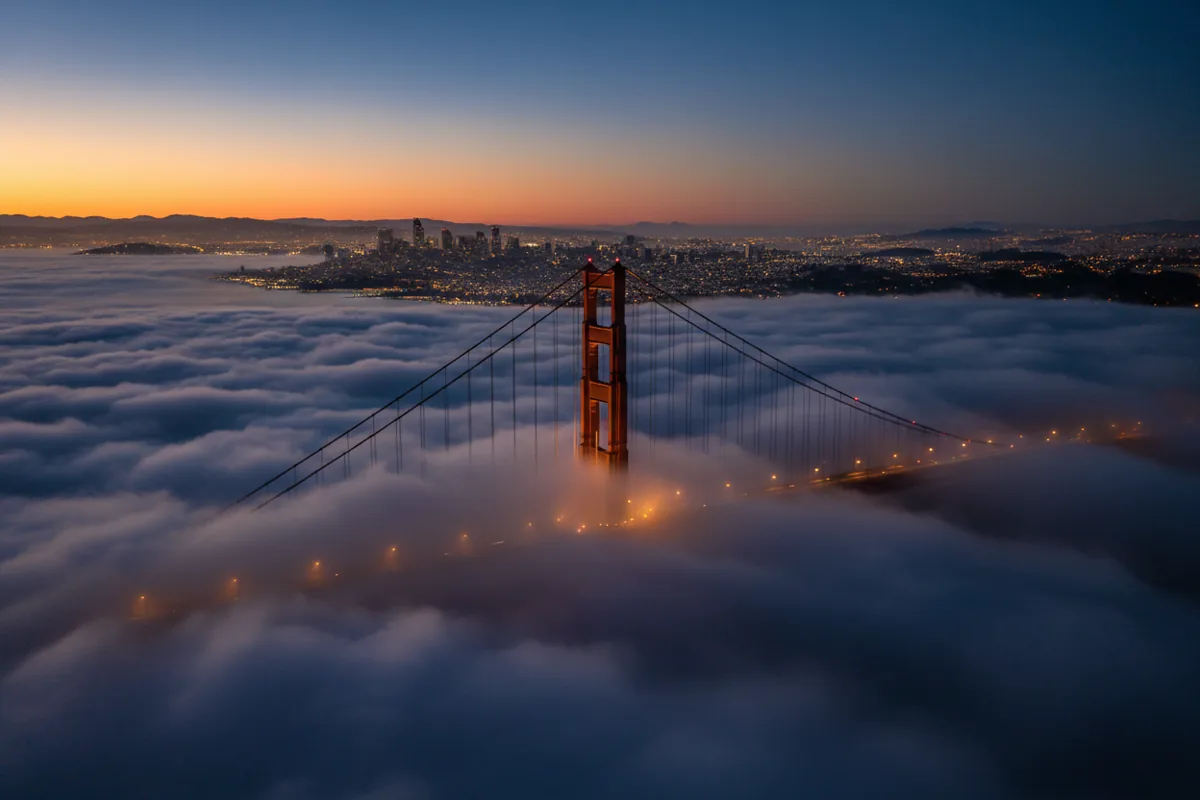 Aerial view of the Golden Gate Bridge and San Francisco emerging from fog at twilight.