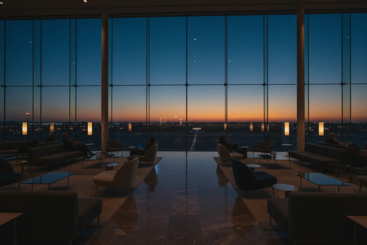 A modern airport lounge with large windows overlooking the tarmac at dusk.
