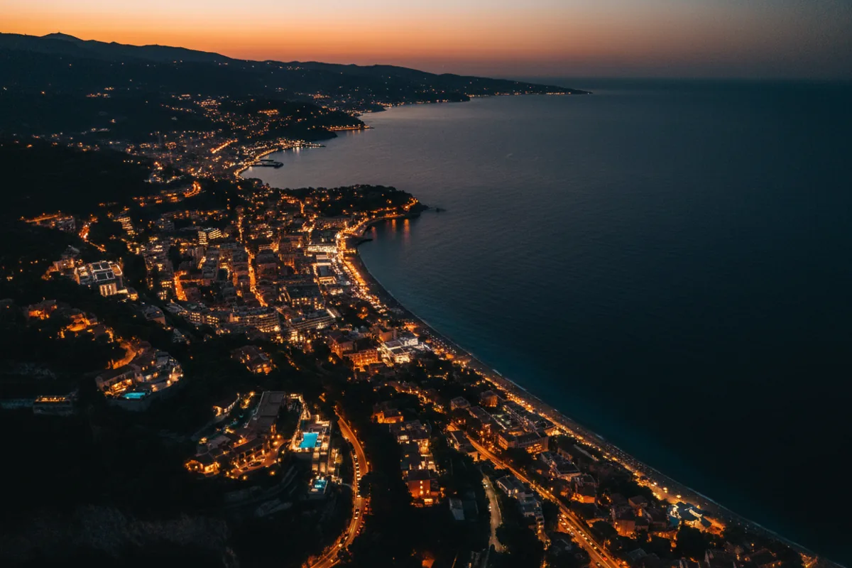 Vue aérienne de la Côte d'Azur au crépuscule depuis un hélicoptère, montrant le littoral illuminé.