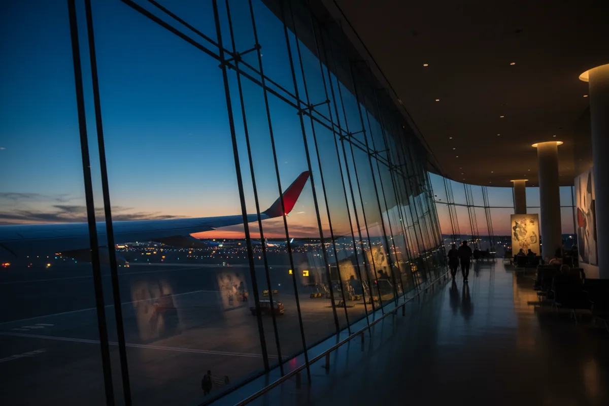 View of an airplane wing on the tarmac at dusk from inside a modern airport terminal.