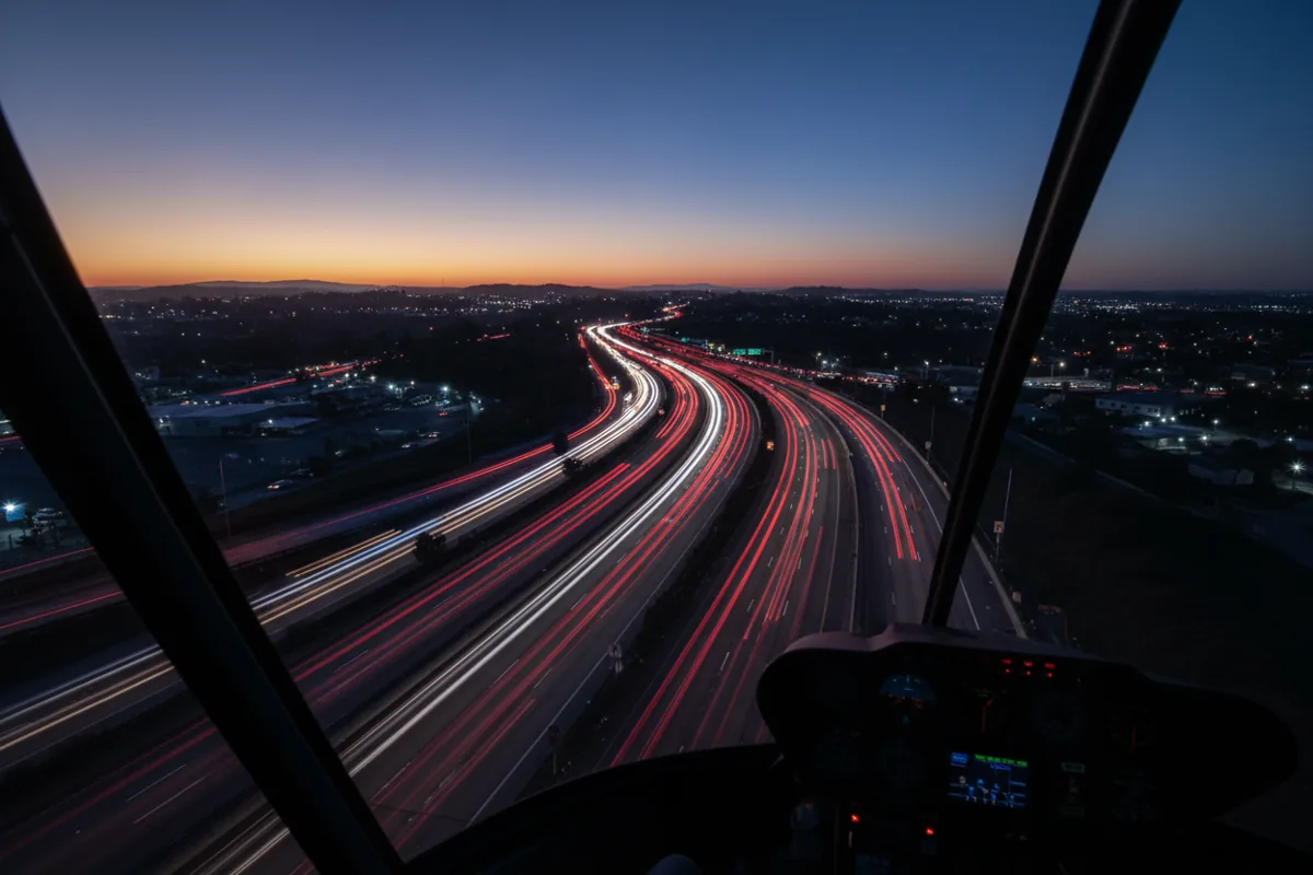 An aerial view from a helicopter at dusk showing light trails from traffic on a highway below.