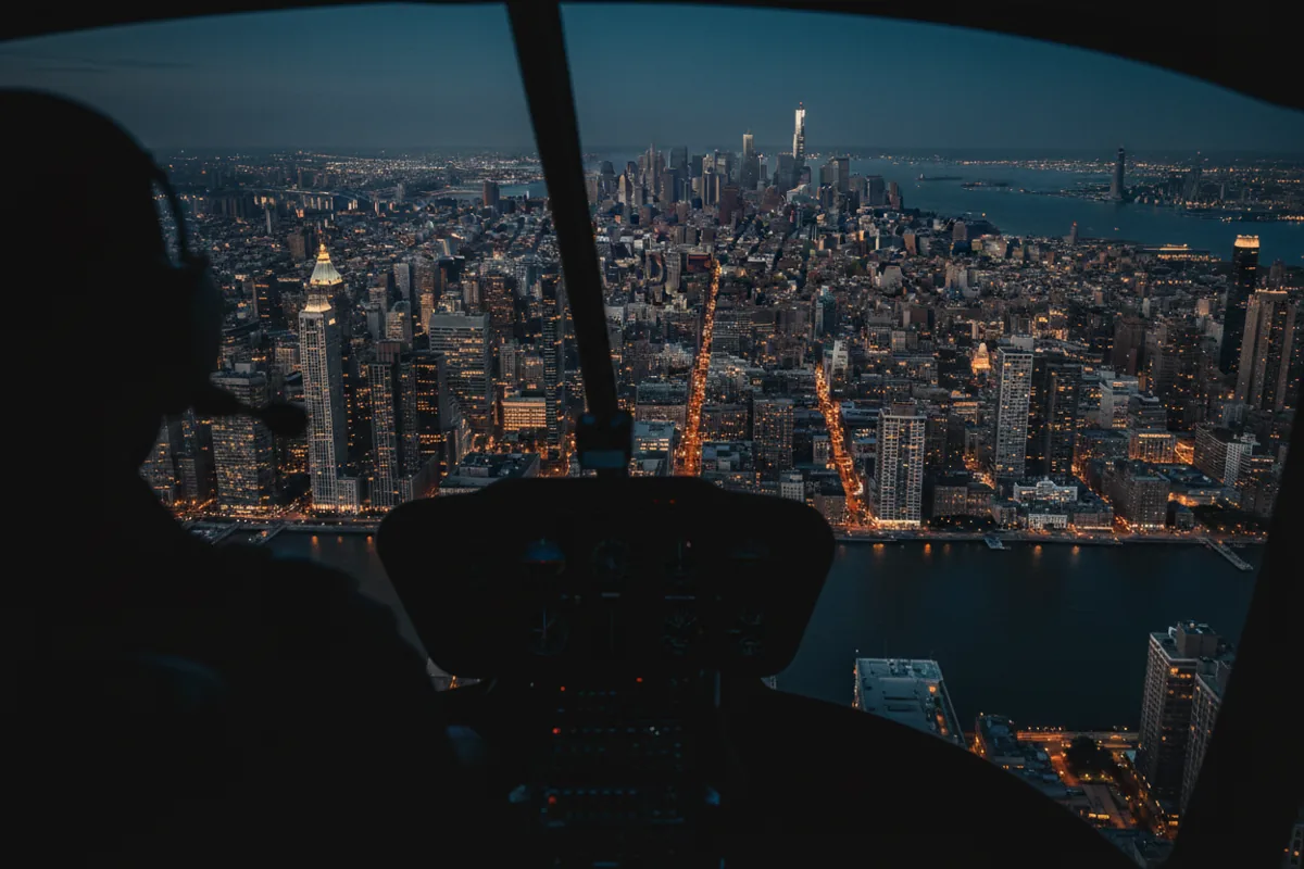 The view from inside a helicopter cockpit flying over Midtown Manhattan at night.