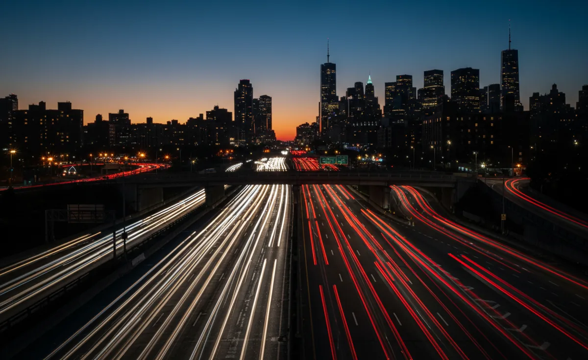Long exposure shot of heavy traffic on a highway leading to a city at dusk.