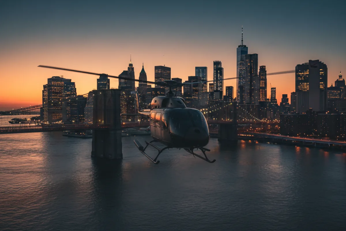 A helicopter flies over the East River at dusk, with the illuminated Lower Manhattan skyline and Brooklyn Bridge in the background.