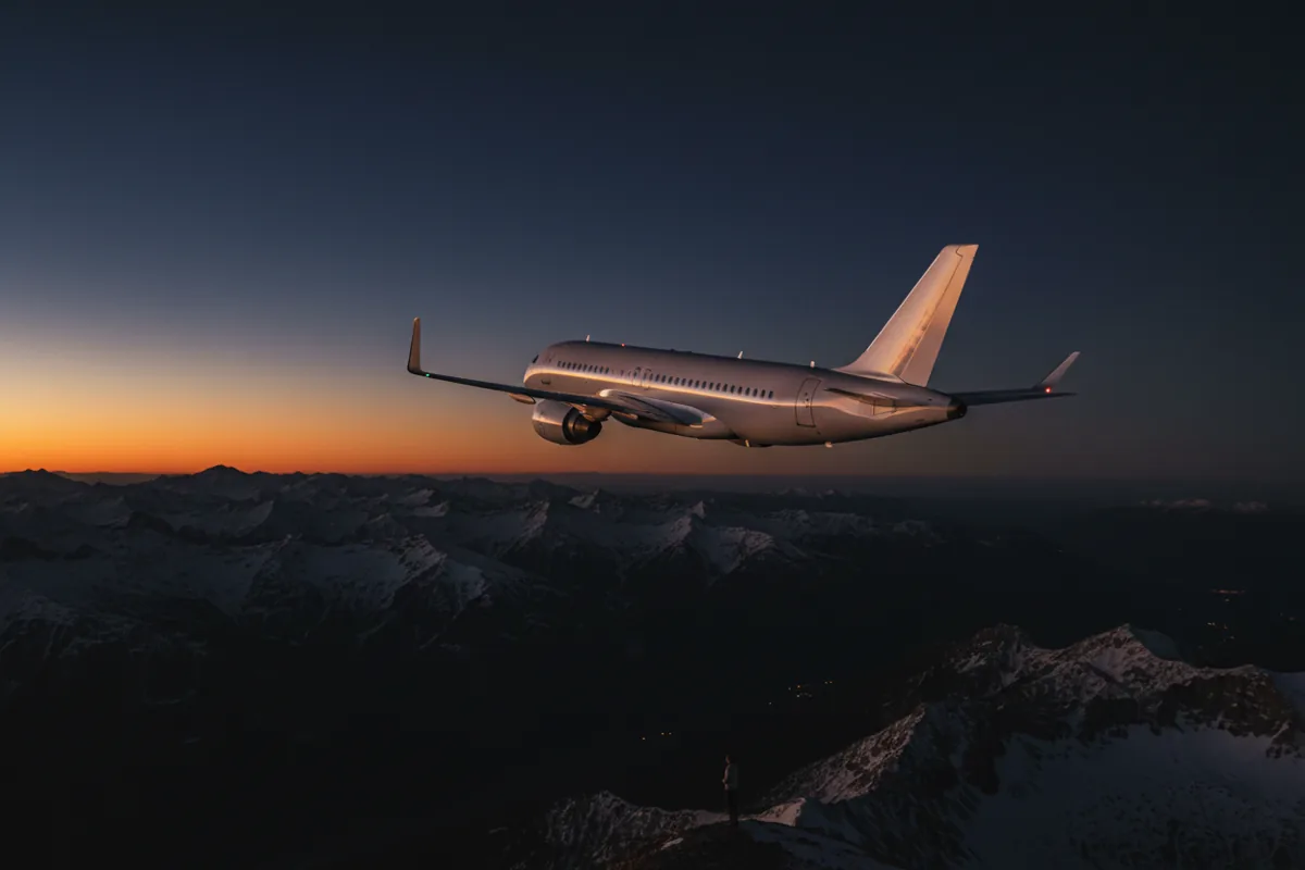 A private jet in flight, banking over mountains at sunset.