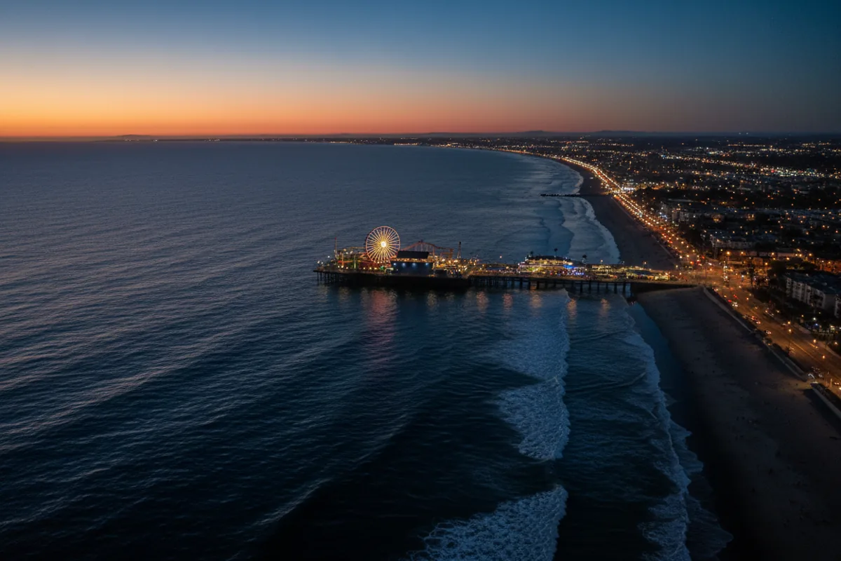 Aerial view of the Santa Monica Pier and coastline at dusk, with lights glowing.