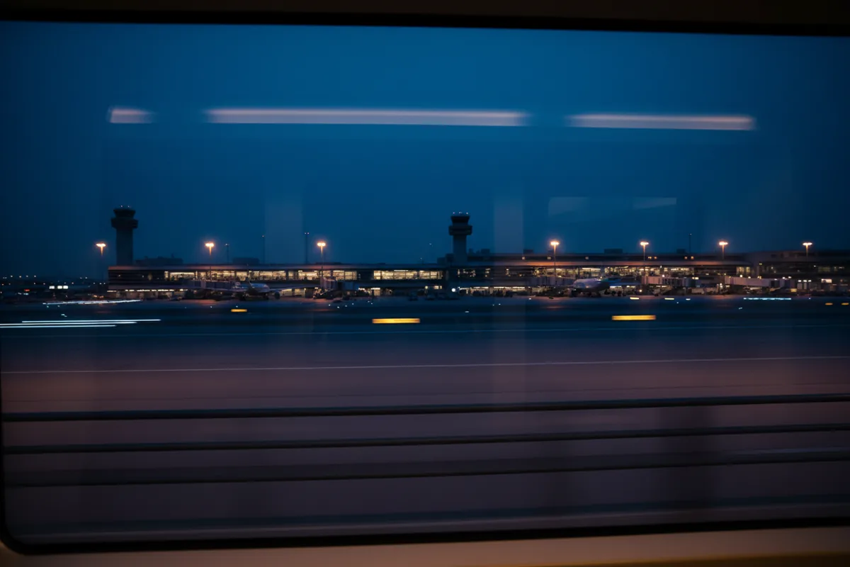 The view of airport terminals and lights at dusk from inside a moving airport train.