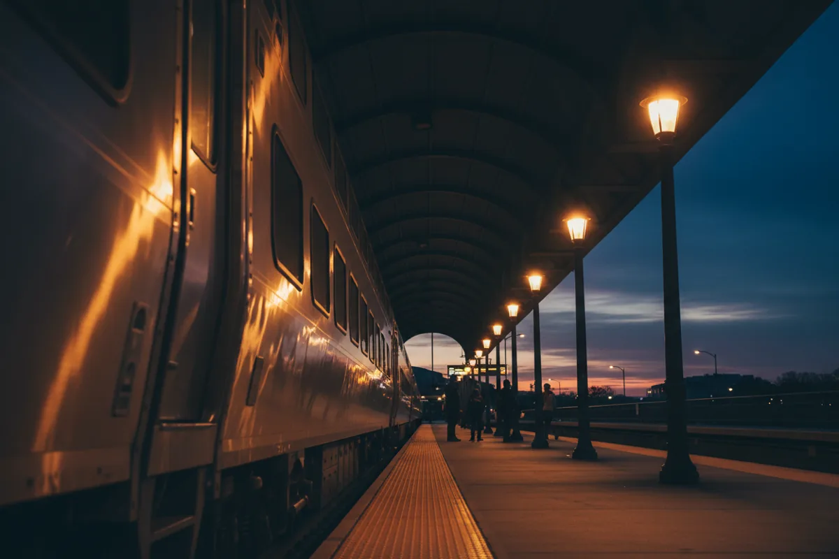 A modern passenger train at a warmly lit platform inside Newark Penn Station.