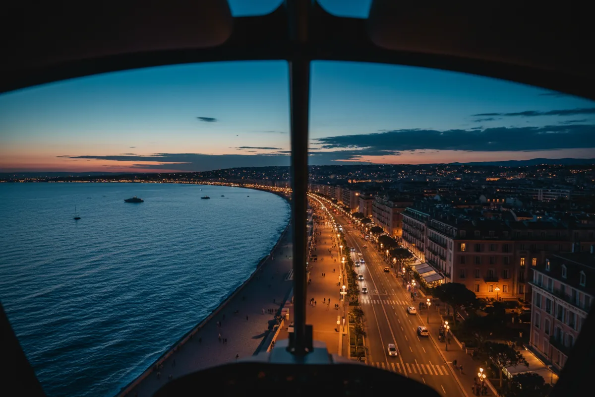 Aerial view from a helicopter of the Nice coastline and the Promenade des Anglais illuminated at dusk.