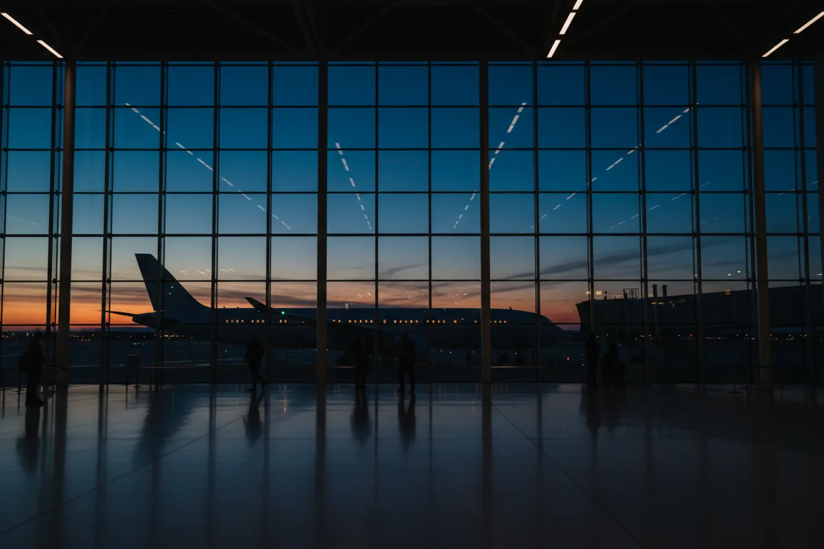 A modern airport terminal at dusk with a passenger jet visible through the window.