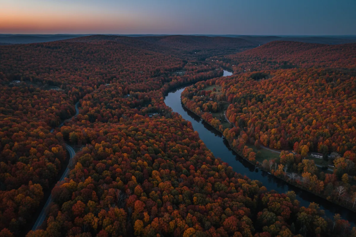 Aerial view of Upstate New York's rolling hills and a river during peak autumn foliage.