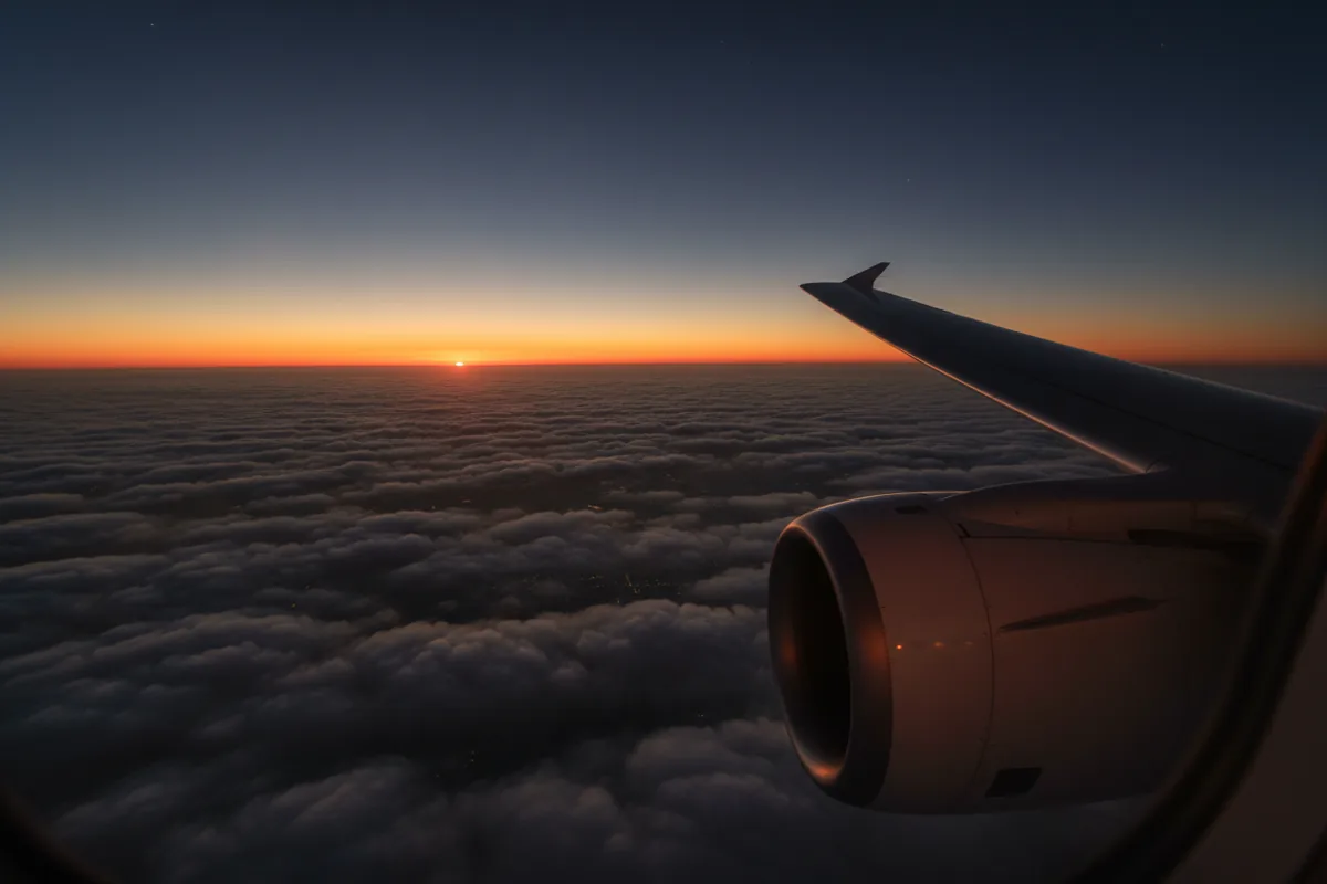 View from an airplane window of the wing over clouds at sunset.