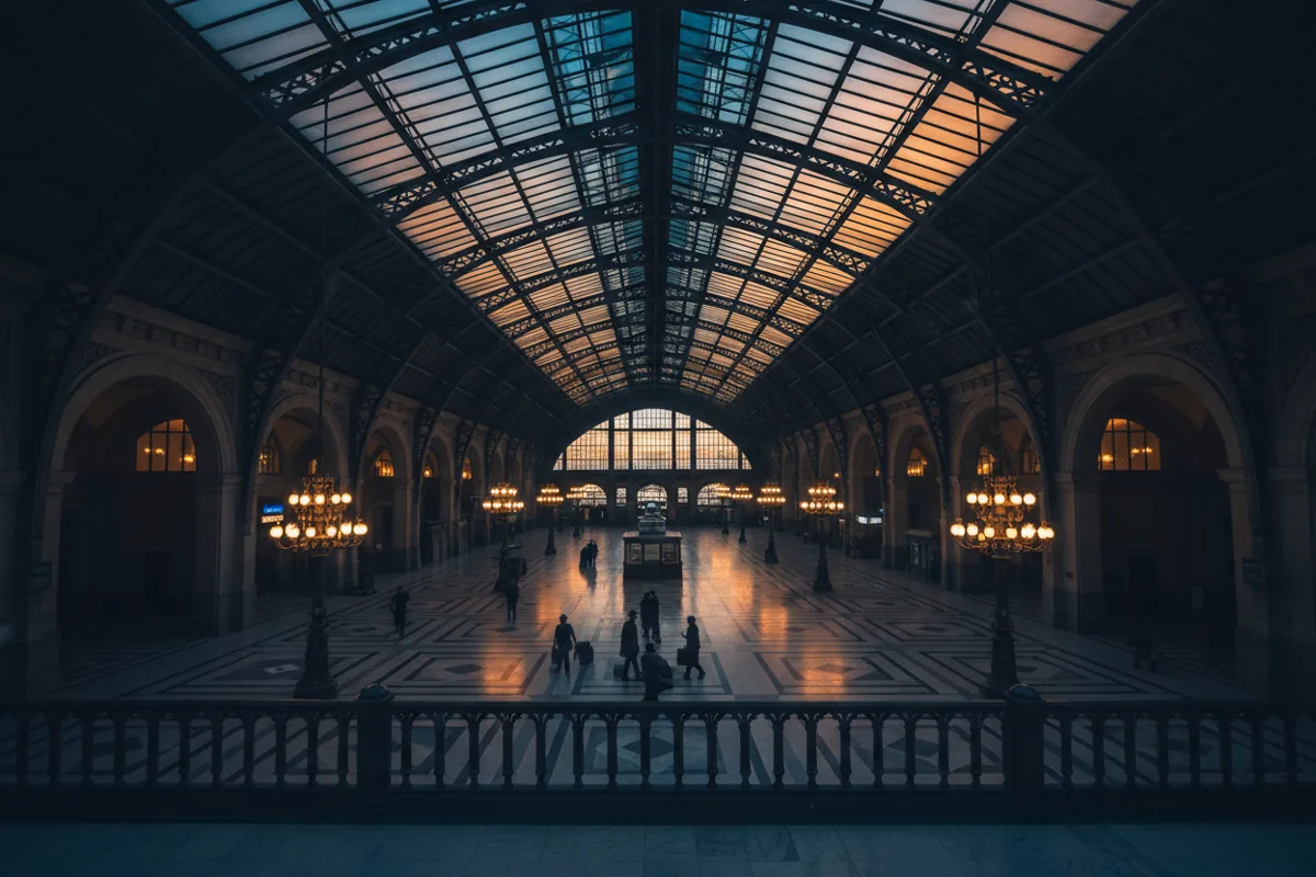 The grand hall of a historic train station with a few travelers at dusk.