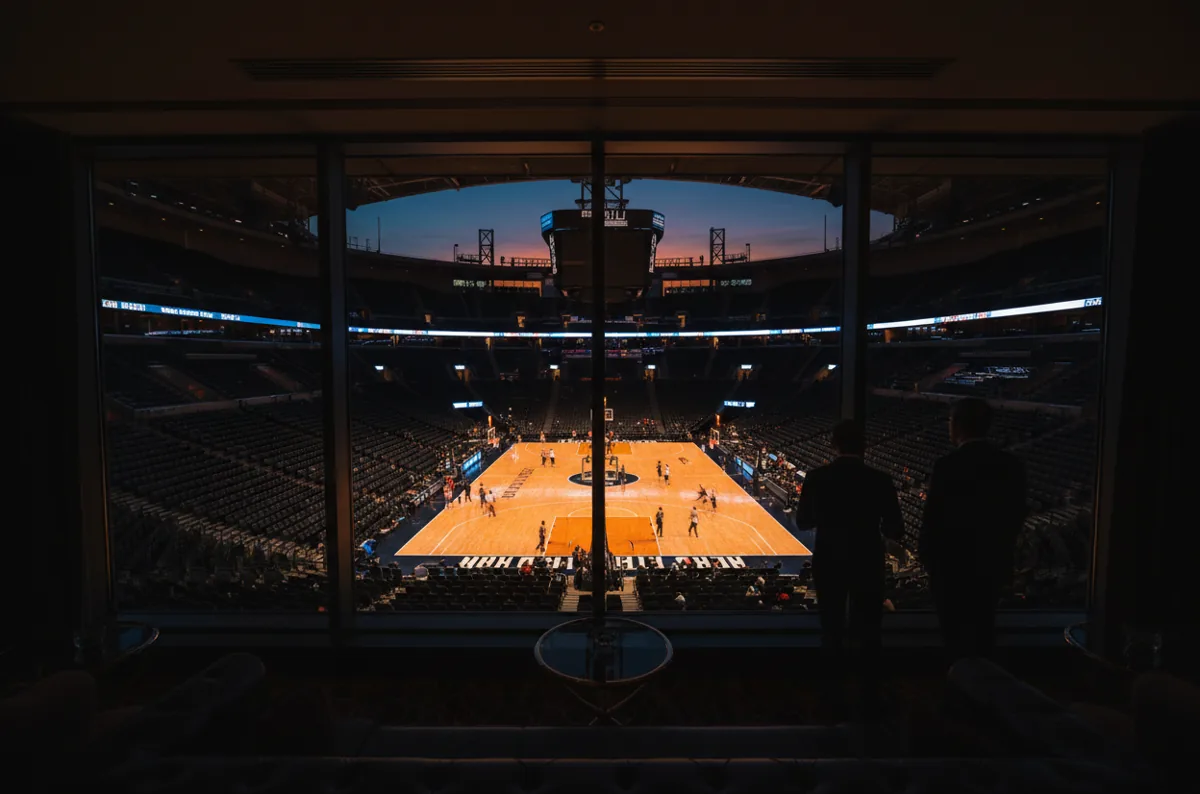 View from a luxury suite overlooking a brightly lit basketball game in a large arena at night.