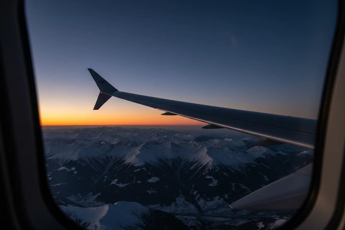 The wing of a private jet flying high above the snow-covered European Alps.