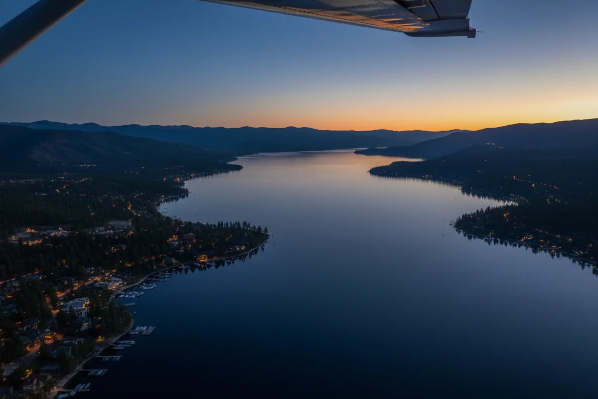 An aerial view of Lake Tahoe at dusk, with lights from shoreline homes visible.