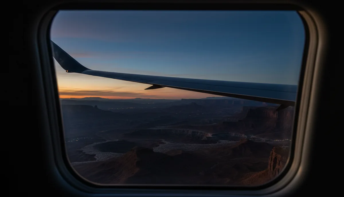 The wing of a private jet seen from the window, flying over a vast desert landscape.