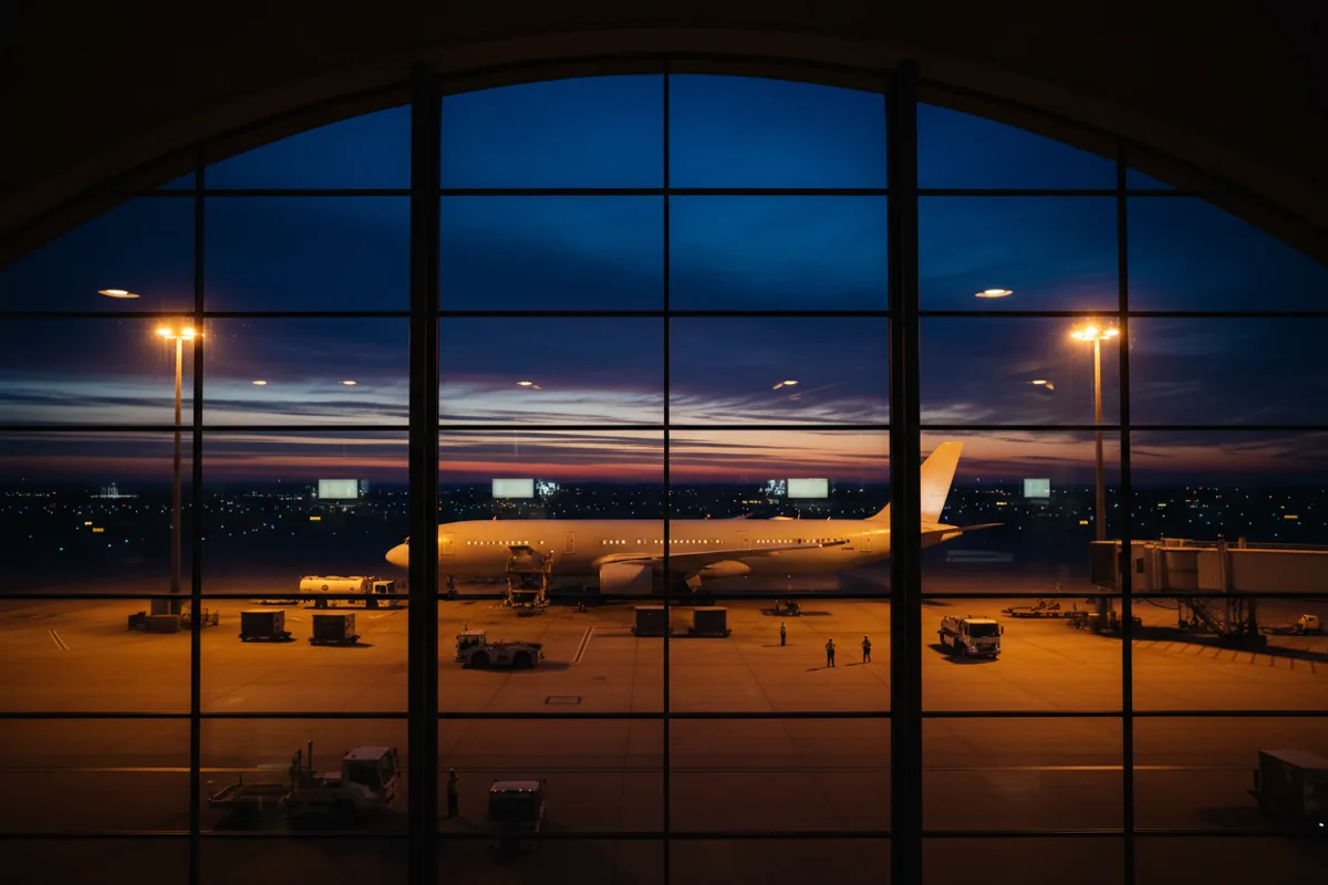 A passenger jet parked at an airport gate at twilight, viewed from inside the terminal.
