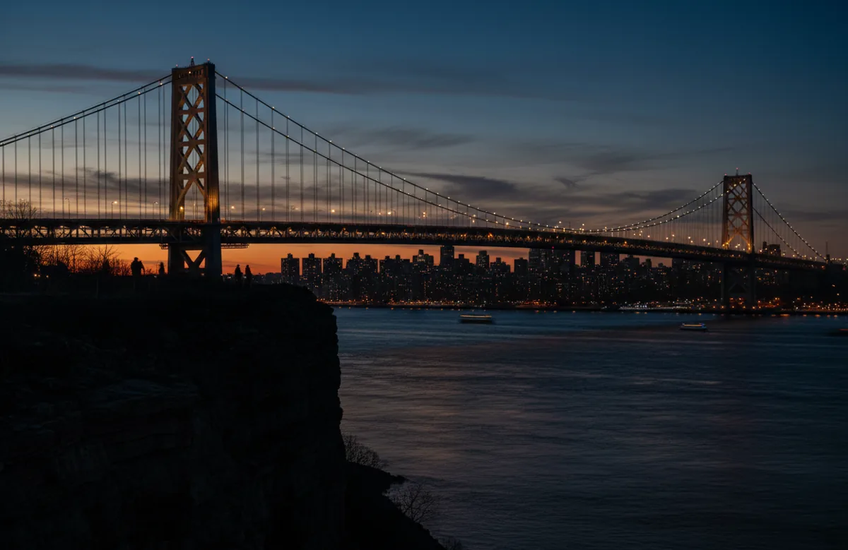 The George Washington Bridge and its lattice towers lit at twilight over the Hudson River.