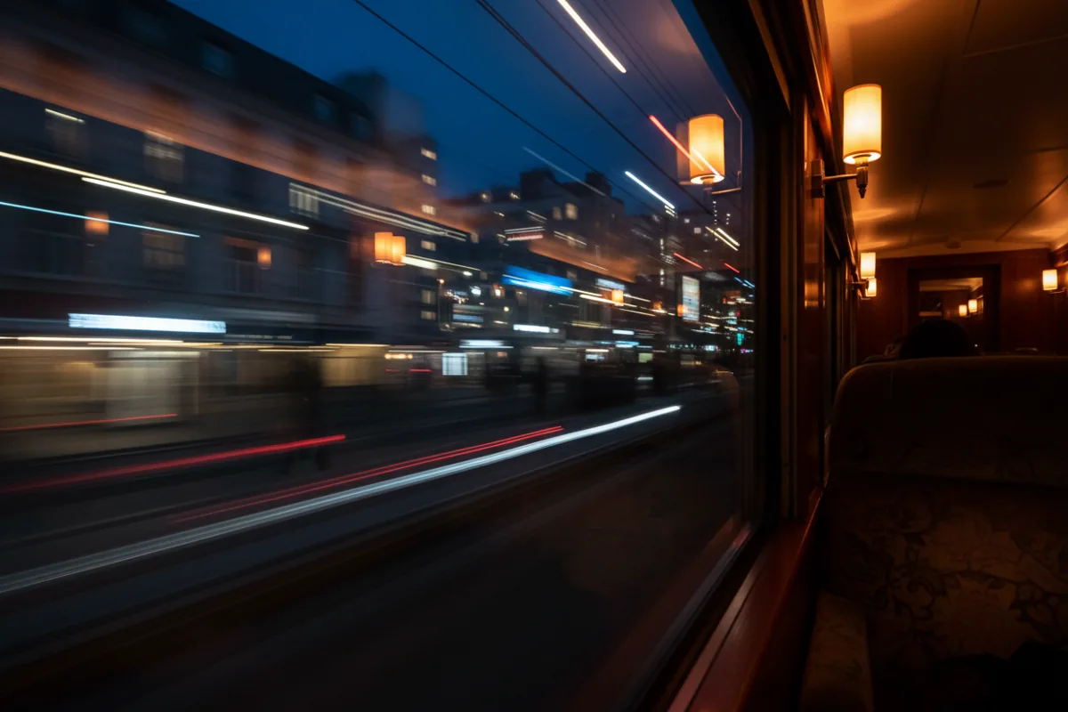 The view of blurred city lights at dusk from a moving train window.