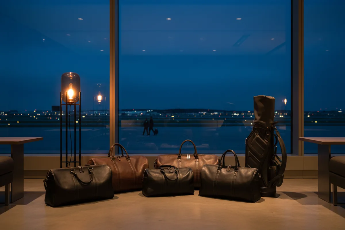 A golf bag and soft-sided luggage sit on the floor of a modern private lounge at twilight.