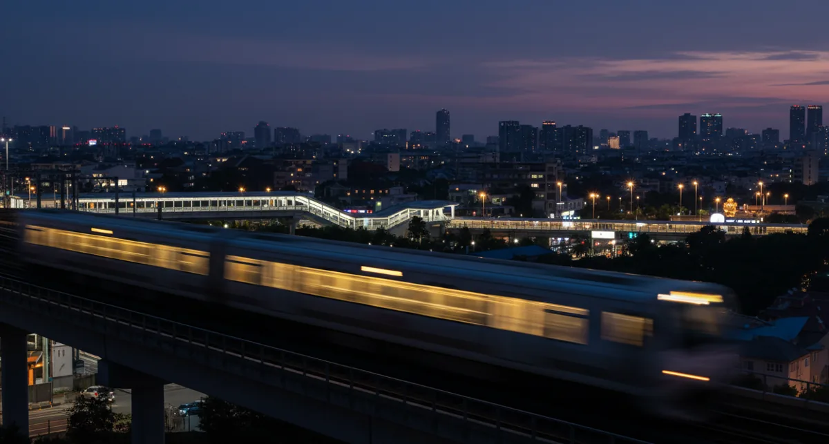 A modern commuter train speeds along tracks at dusk, its interior lights glowing warmly against the dark sky.